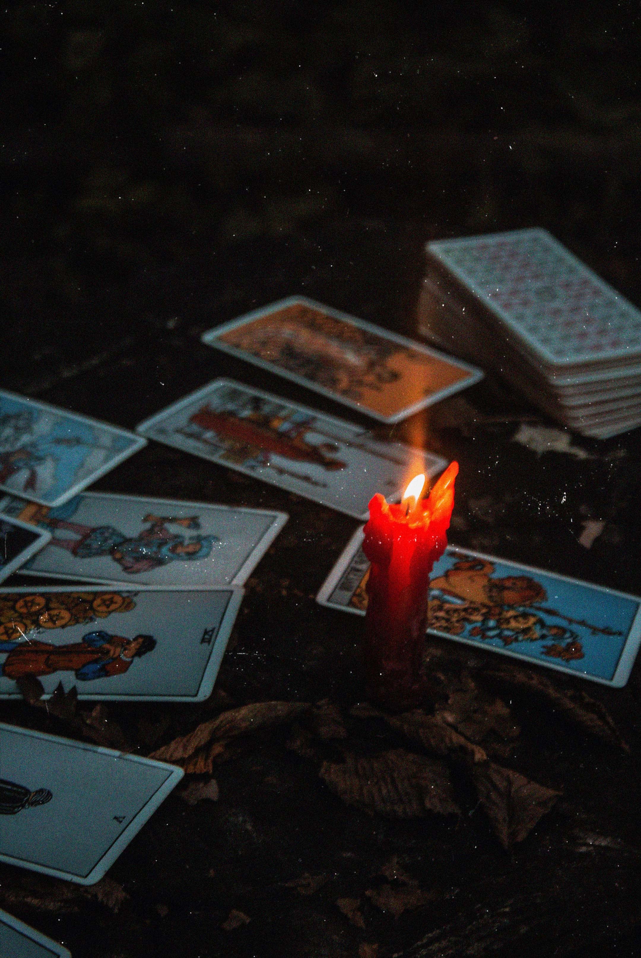 Tarot cards laying on a table, with a lit melting red wax candle.