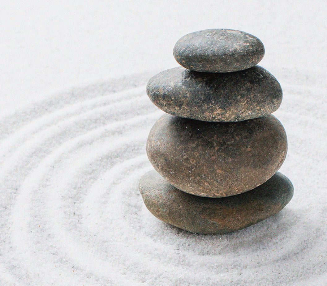 Four round stones balancing on top of eachother, sitting in white sand, representing the work of Wheelhouse, a holistic health and healing studio opening in Lisbon, Portugal.